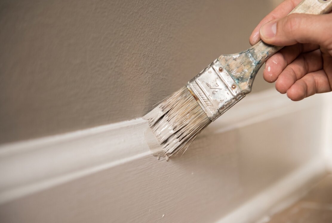 Malerpinsel beim Streichen einer Wand in warmem Grau